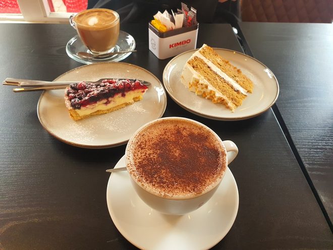 Berry tart, layered cream cake, a cappuccino and a latte on a dark table, cropped so the burned-in wording is out of frame