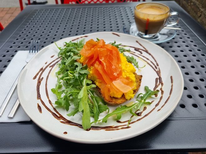 Salmon and scrambled egg on toast on an outdoor table with an espresso