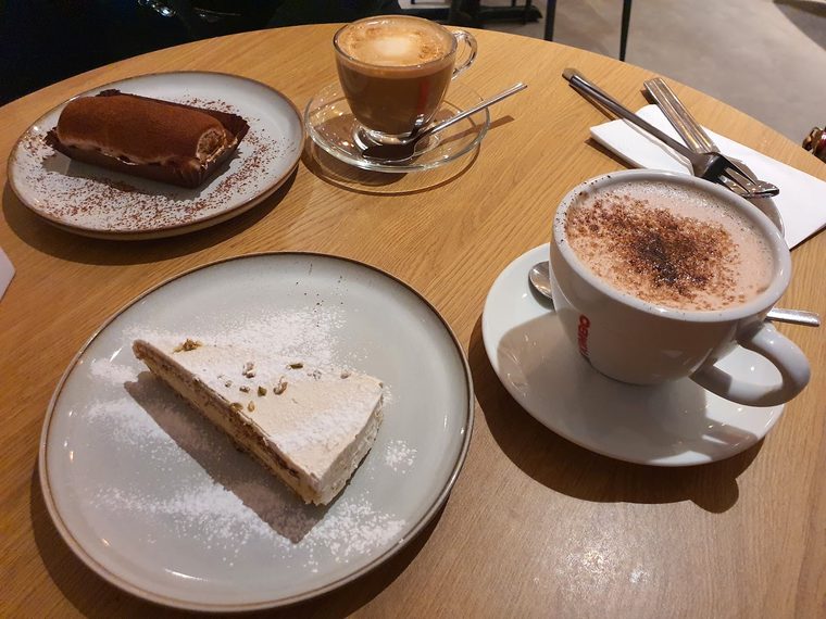 A plain cheesecake slice beside a chocolate-topped cake slice, with a cappuccino